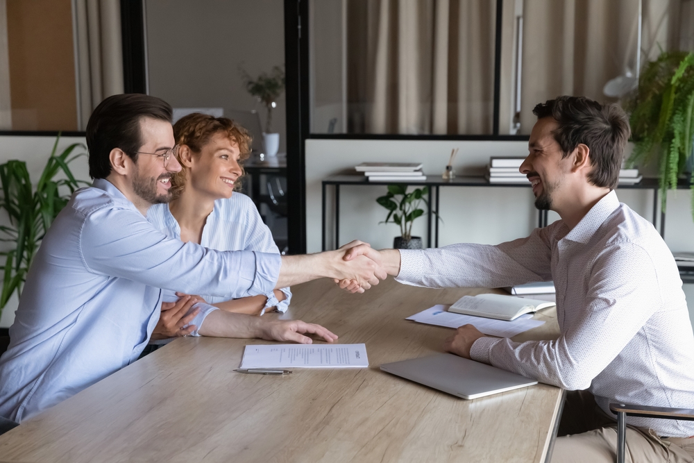 couple shaking hand with man over table for settling debt